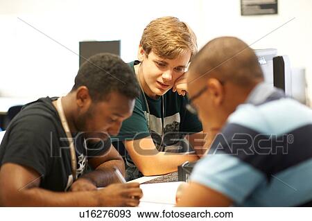 Stock Image - Male higher education students looking at paperwork in college classroom. Fotosearch