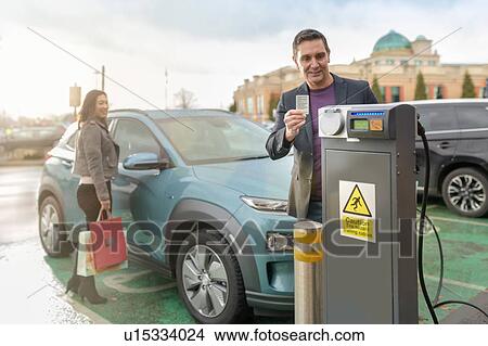 Picture - Man and woman charging electric car at car charging park, Manchester, UK. Fotosearch