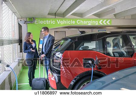 Stock Photo - Man and woman charging electric car at charge bay, Manchester, UK. Fotosearch