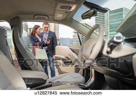 Stock Photography - Man and woman checking car charge on mobile phone app, Manchester, UK. Fotosearch