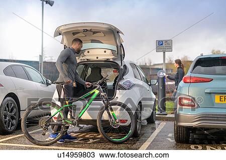 Stock Image - Man and woman with mountain bike at electric car charging point, Manchester, UK. Fotosearch