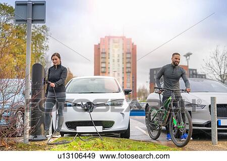 Man and woman with mountain bike at electric car charging point, Manchester, UK View Large Photo Image Stock Photo - Man and woman with mountain bike at electric car charging point, Manchester, UK. Fotosearch