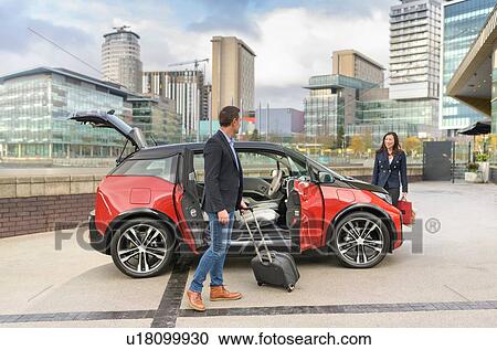 Stock Image - Man and woman with parked electric car, Manchester, UK. Fotosearch