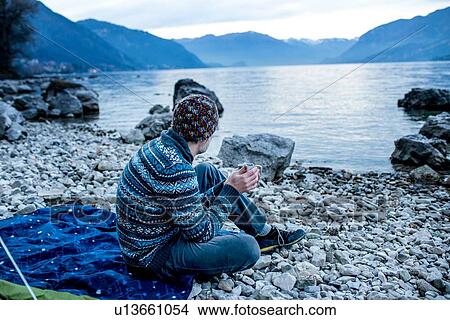 Picture - Man camping on lakeside, Onno, Lombardy, Italy. Fotosearch