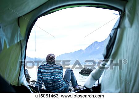 Stock Image - Man camping on lakeside, view from inside tent, Onno, Lombardy, Italy. Fotosearch