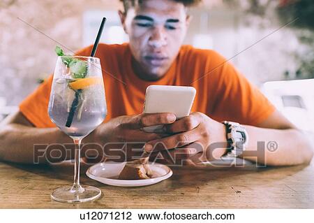 Stock Image - Man texting and having drink in bar. Fotosearch