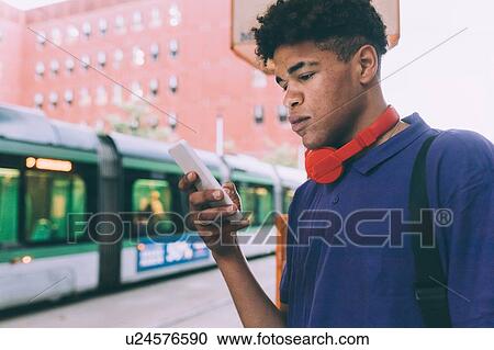 Stock Image - Man texting at tram stop, Milan, Italy. Fotosearch