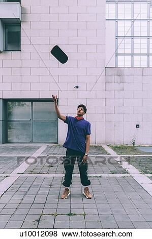 Stock Photo - Man throwing skateboard into air, Milan, Italy. Fotosearch