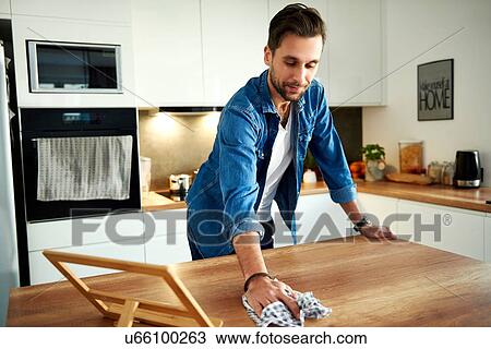 Stock Image - Man wiping table in kitchen. Fotosearch