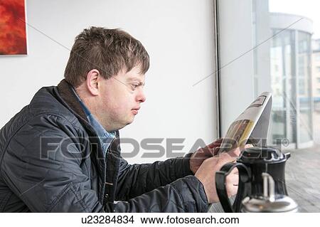 Picture - Man with down syndrome reading newspaper by cafe window. Fotosearch