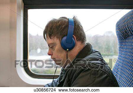 Picture - Man with down syndrome using headphones on train. Fotosearch
