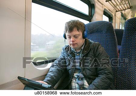 Stock Photo - Man with down syndrome using headphones and digital tablet on train. Fotosearch