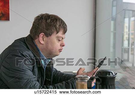 Stock Photography - Man with down syndrome using phone by cafe window. Fotosearch