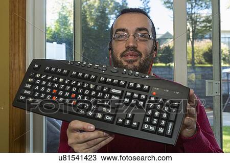 Stock Image - Man with visual impairment holding up his adaptive keyboard. Fotosearch