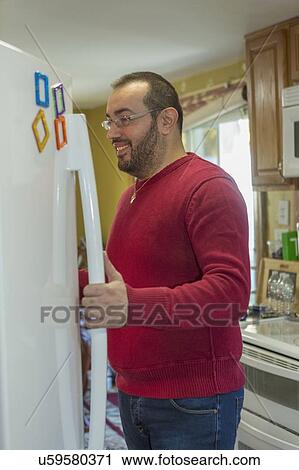 Stock Image - Man with visual impairment opening refrigerator. Fotosearch