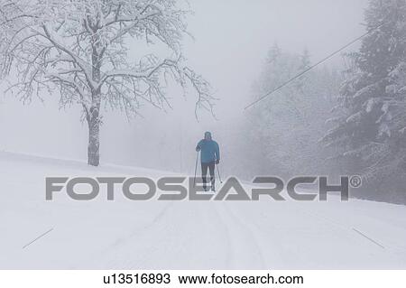 Stock Image - Mature man cross country skiing by misty forest, full length. Fotosearch