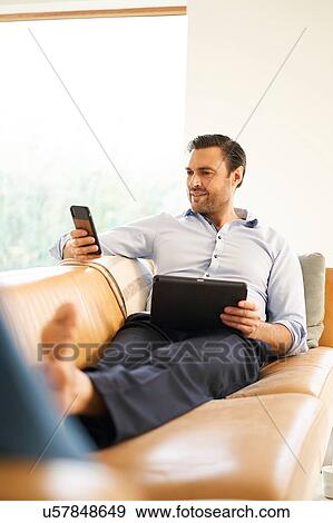 Mature man looking at smartphone whilst reclining on sofa View Large Photo Image Stock Photo - Mature man looking at smartphone whilst reclining on sofa. Fotosearch
