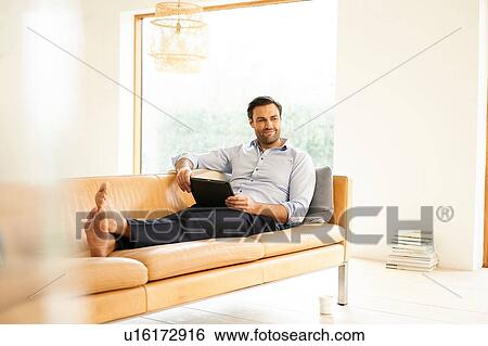 Stock Photograph - Mature man with digital tablet reclining on sofa. Fotosearch