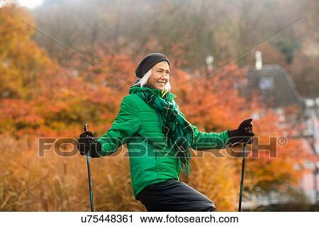 Stock Image - Mature woman nordic walking in park. Fotosearch