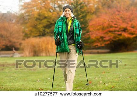 Stock Photo - Mature woman nordic walking in park. Fotosearch