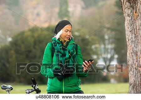Stock Photograph - Mature woman using smartphone in park. Fotosearch