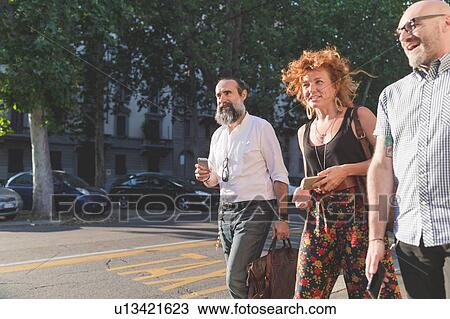 Mid adult woman and male friends chatting while strolling on city sidewalk View Large Photo Image Stock Image - Mid adult woman and male friends chatting while strolling on city sidewalk. Fotosearch