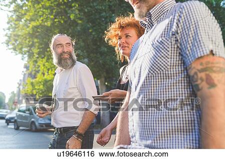Mid adult woman and male friends chatting while strolling on city street View Large Photo Image Stock Photograph - Mid adult woman and male friends chatting while strolling on city street. Fotosearch