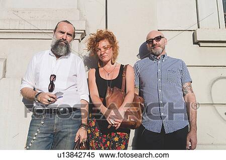 Stock Photography - Mid adult woman and male friends leaning against wall in city, portrait. Fotosearch