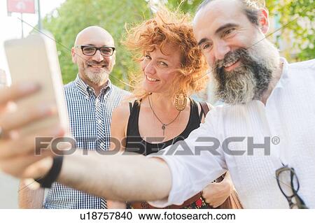 Mid adult woman and male friends taking smartphone selfie on city street View Large Photo Image Stock Image - Mid adult woman and male friends taking smartphone selfie on city street. Fotosearch