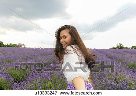 Mid adult woman with long brown hair looking over her shoulder in lavender field View Large Photo Image Stock Photo - Mid adult woman with long brown hair looking over her shoulder in lavender field. Fotosearch