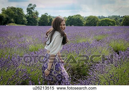 Stock Photography - Mid adult woman with long brown hair looking over her shoulder in lavender field, portrait. Fotosearch