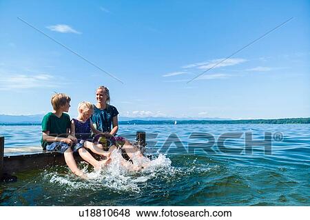 Stock Photo - Mother and children cooling feet in water, Lake Starnberg, Bavaria, Germany. Fotosearch