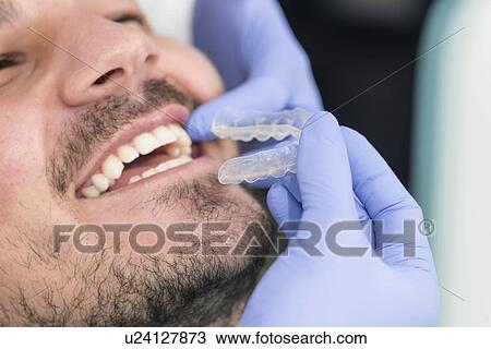 Stock Image - Orthodontist fitting invisible braces. Fotosearch