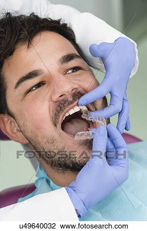 Stock Image - Orthodontist fitting invisible braces. Fotosearch