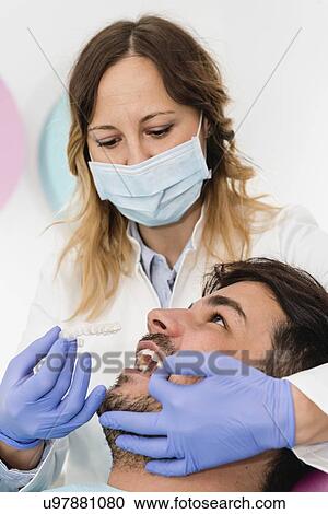 Stock Image - Orthodontist fitting invisible braces. Fotosearch