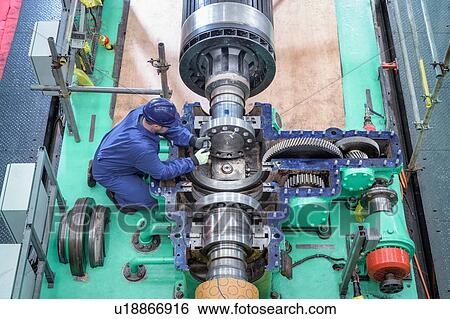 Stock Photograph - Overhead view of engineer inspecting gears on generator in turbine hall of nuclear power station during outage. Fotosearch