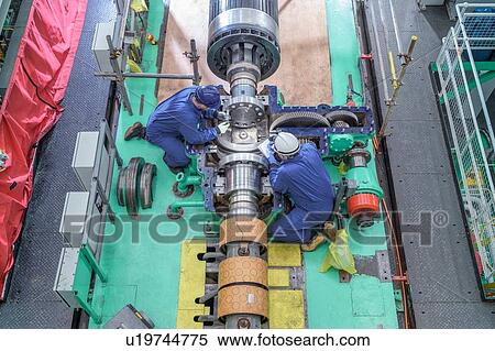 Stock Photography - Overhead view of engineers inspecting gears on generator in turbine hall of nuclear power station during outage. Fotosearch