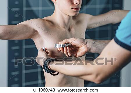Stock Image - Physical therapist measuring teenage boy's chest. Fotosearch