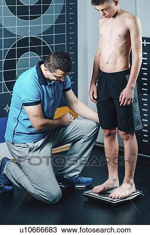 Stock Image - Physical therapist measuring weight of teenage boy. Fotosearch