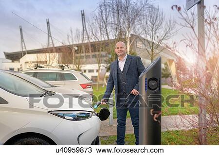 Portrait of businessman plugging in electric car at charging point, Manchester, UK View Large Photo Image Stock Image - Portrait of businessman plugging in electric car at charging point, Manchester, UK. Fotosearch