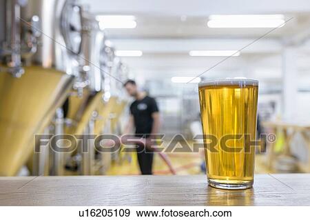 Stock Photo - Portrait of glass of beer in brewery, brewer with pipe in background. Fotosearch