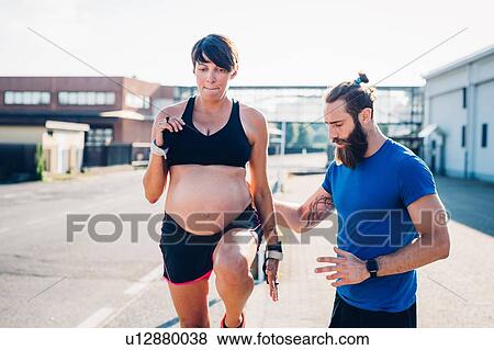 Stock Photo - Pregnant woman and personal trainer working out outdoors. Fotosearch