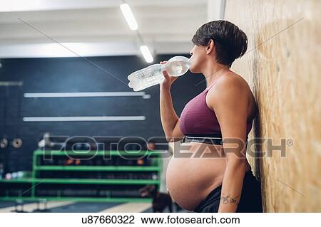 Pregnant woman drinking from water bottle in gym View Large Photo Image Stock Image - Pregnant woman drinking from water bottle in gym. Fotosearch