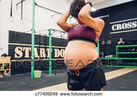 Stock Photo - Pregnant woman holding head in hand in gym. Fotosearch