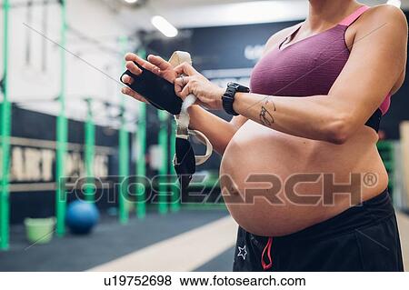 Pregnant woman putting on workout gloves in gym View Large Photo Image Stock Photo - Pregnant woman putting on workout gloves in gym. Fotosearch