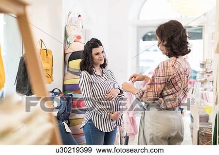 Stock Photo - Pregnant woman shopping for baby clothes. Fotosearch