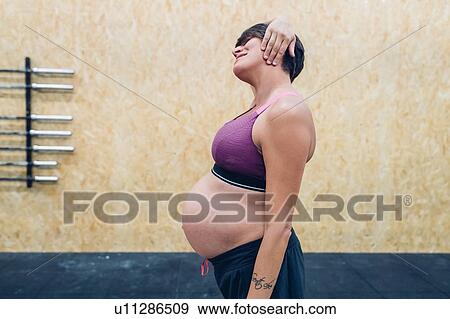 Stock Photo - Pregnant woman trying to touch ears in gym. Fotosearch