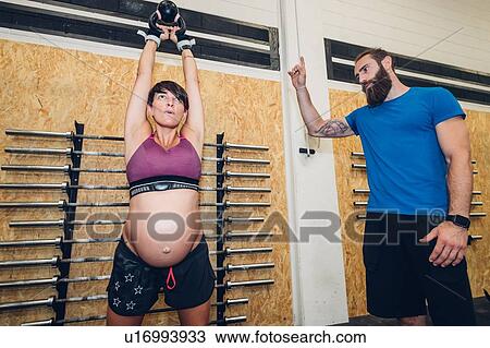 Stock Image - Pregnant woman using kettlebell in gym. Fotosearch