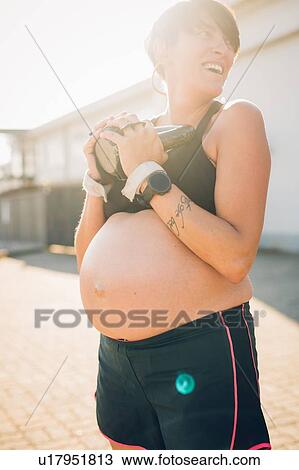 Stock Image - Pregnant woman using kettlebell outdoors. Fotosearch