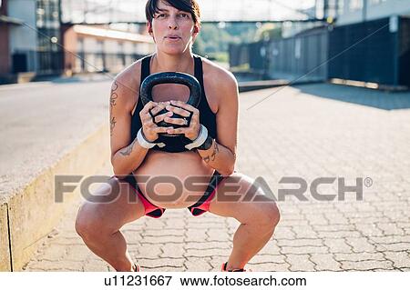 Stock Photo - Pregnant woman using kettlebell outdoors. Fotosearch